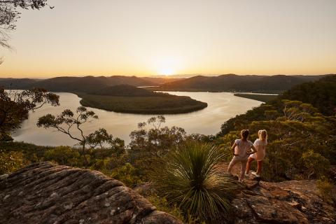 women standing high on a bush rock overlooking expanse of bush and river 