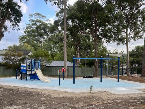 A photo of Ben Davis Reserve in Bensville with a play unit with a slide, climbing wall and shop counter, standard swing, nest swing, bike track, flying fox, rubber softfall, park furniture and pathway. 