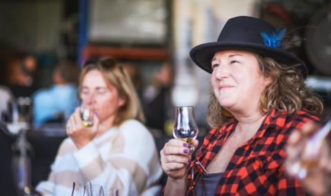 A woman in a hat and plaid shirt holding a glass of wine.