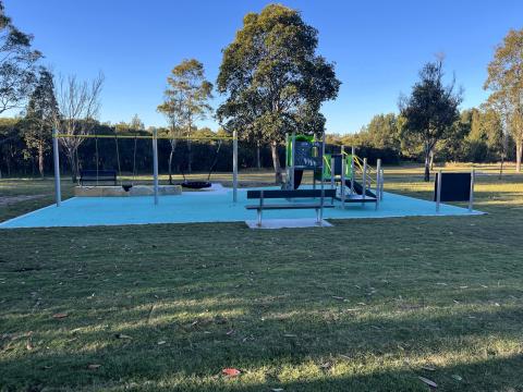 A photo of a playspace in Oregon Place Reserve, Hamlyn Terrace with a slide, net climber, rocker, spinner, sensory play panels, standard swing, nest swing and junior swing, rubber softfall and pathway.