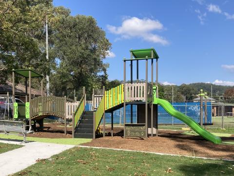 A photo of the playspace in Maidens Brush Reserve in Wyoming which includes three slides, a climbing wall and shop counter, a rocker, nest swing, rubber and mulch softfall and a new path linking to the car park. It also includes the addition of a disabled parking spot.