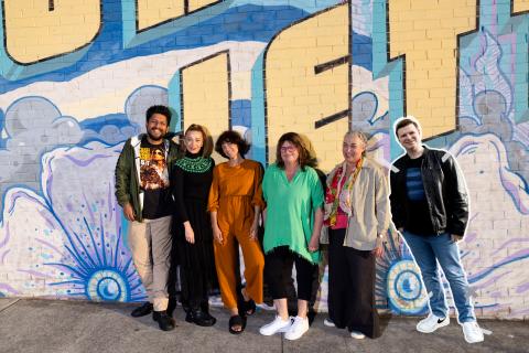 Group photo of the recipients of Creative Art Central commissioning program 2023-24 standing in front of a graffitied wall in Long Jetty.