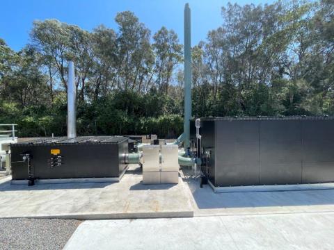 A large industrial facility featuring two prominent black tanks against a clear sky backdrop.