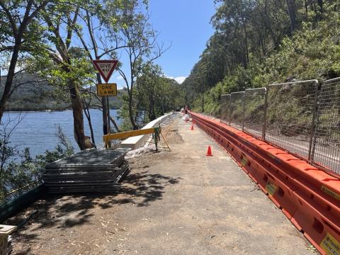 Site on Wisemans Ferry Road with active construction works in progress, one traffic lane on right and Hawkesbury River on left