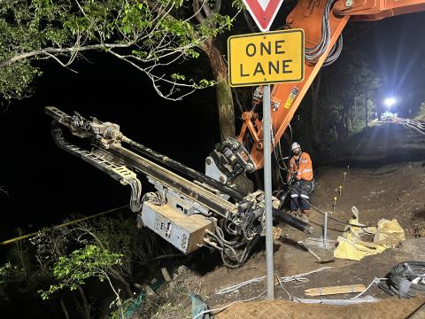 Construction worker using heavy machinery at night at site on Wisemans Ferry Road, plus One Lane traffic sign 